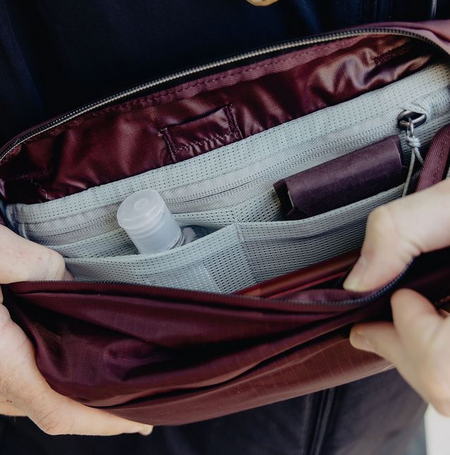 Blick in das geöffnete, hellgraue Innenfach einer weinroten Peak Design Everyday Sling V2 Kameratasche (in der Farbvariante Eclipse), die von zwei Händen offengehalten wird. Das Bild zeigt das flexible Organisationssystem des Hauptfachs, bestehend aus meh