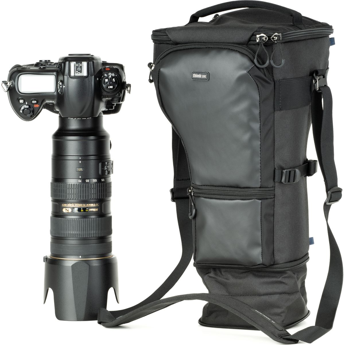 Schwarzes Kamera-Holster mit Schultergurt neben einer Kamera mit großem Teleobjektiv und Gegenlichtblende.